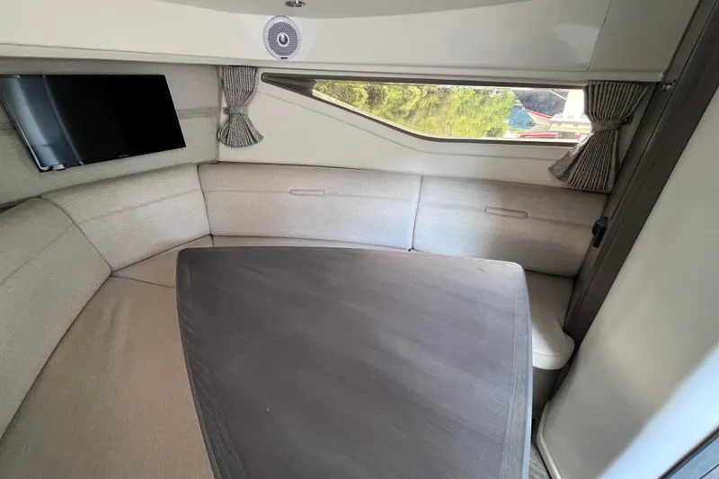 Slide: The Image of 2020 Sea Ray Sundancer 320 Outboard cabin interior with seating, table, and window view. - 57