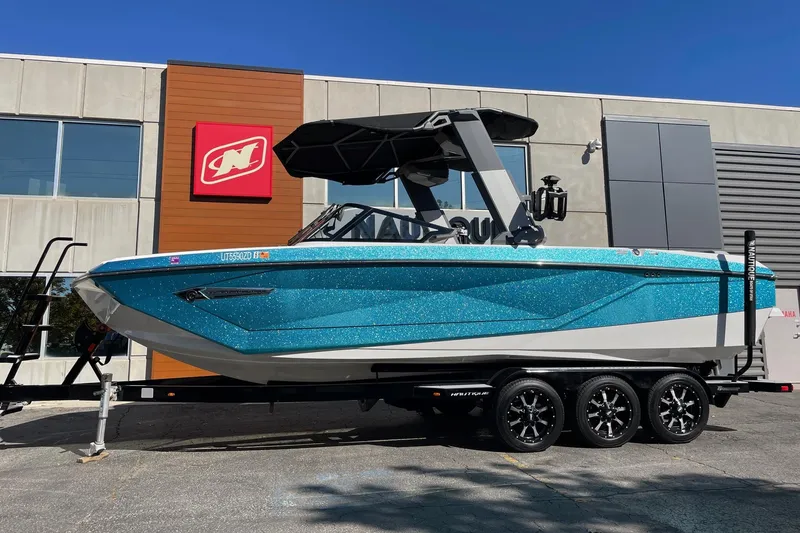 The Image of 2022 Nautique Super Air Nautique G25 boat in vibrant blue on a trailer outside a dealership. - 1