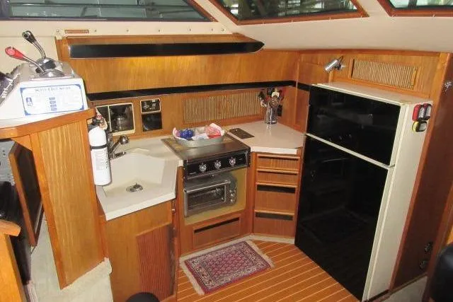 Slide: The Image of 1988 Sea Ray 415 Aft Cabin kitchen with stove, fridge, and wooden cabinetry. - 31