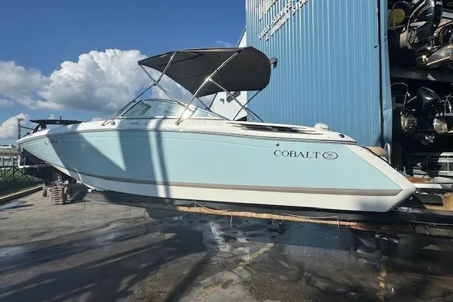 Slide: The Image of 2015 Cobalt 26SD boat with canopy, docked near a blue building under a clear sky. - 6