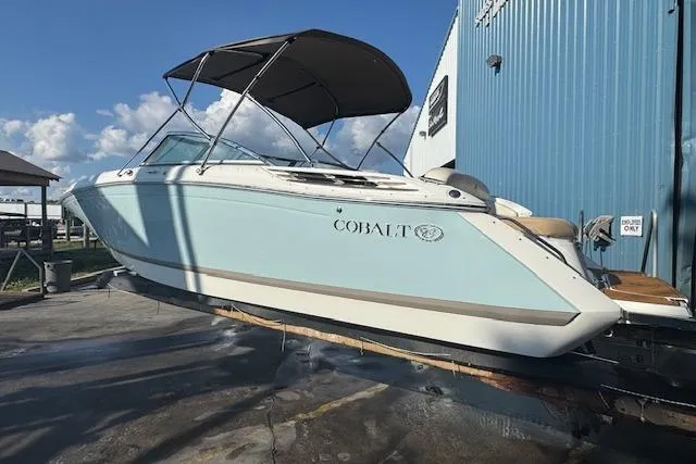 Slide: The Image of 2015 Cobalt 26SD boat with canopy, docked near blue building under clear sky. - 8