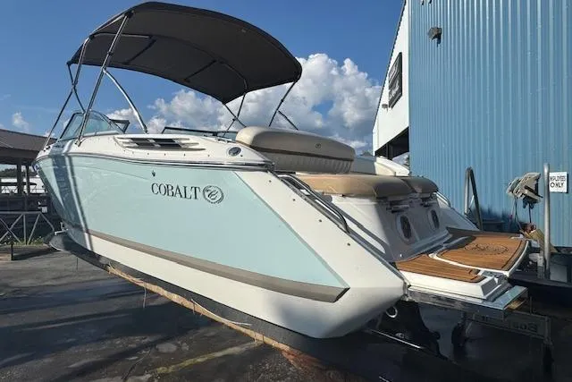 Slide: The Image of 2015 Cobalt 26SD boat with canopy, docked near a blue building under a clear sky. - 9