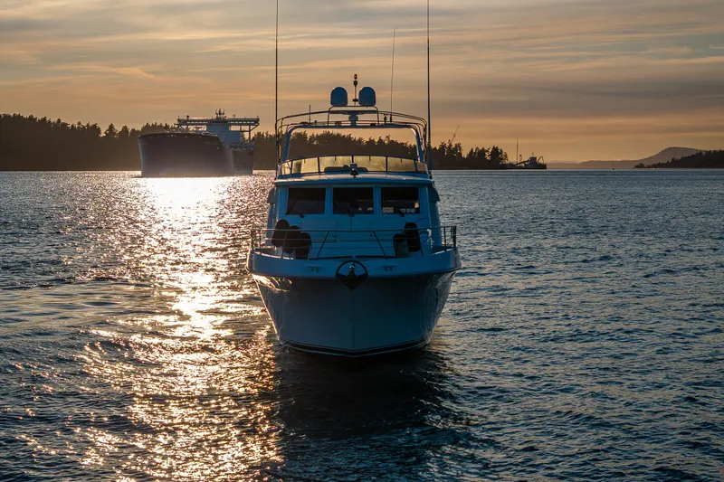 Slide: The Image of 2001 Navigator 61' Pilothouse yacht on serene water at sunset, with distant ship. - 13