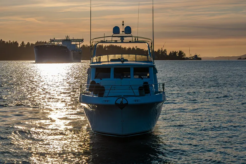 Slide: The Image of 2001 Navigator 61' Pilothouse yacht on serene water at sunset, with distant ship. - 14