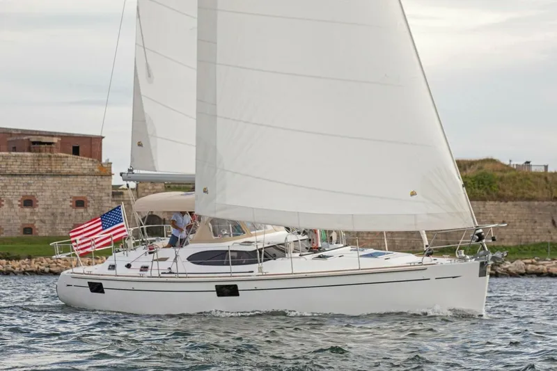 The Image of 2025 Hylas H48 sailboat with American flag, sailing near a historic stone building. - 1
