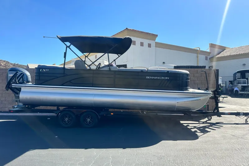 The Image of 2022 Bennington LX 24 L-Bench pontoon boat on trailer, parked outdoors. - 0