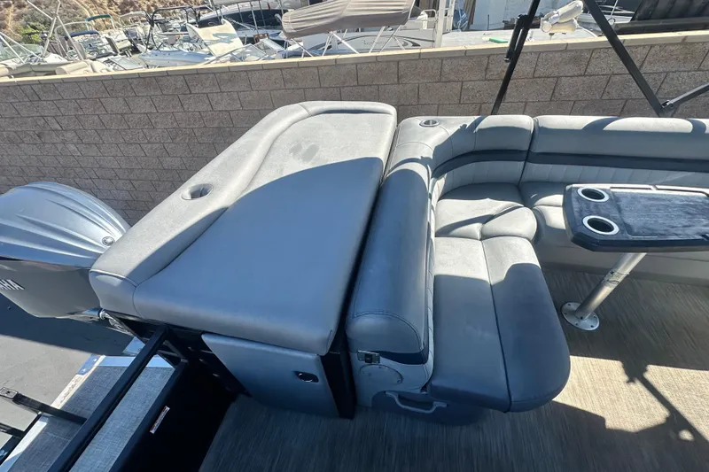 Slide: The Image of 2022 Bennington LX 24 L-Bench pontoon boat with gray seating and table, docked at marina. - 12
