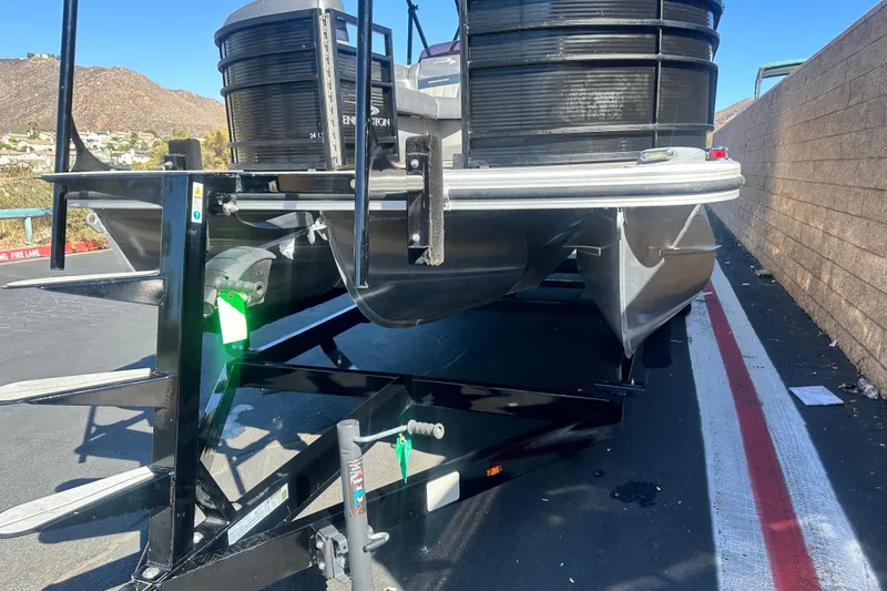 Slide: The Image of 2022 Bennington LX 24 L-Bench pontoon boat on trailer, parked near a wall. - 2