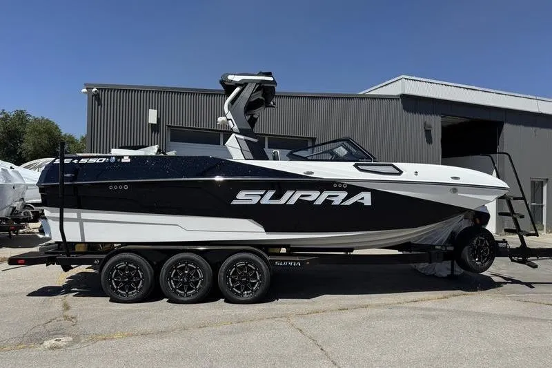 The Image of 2025 Supra SE 575 boat on trailer, parked outside industrial building. - 0