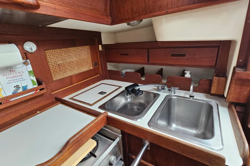 Slide: The Image of 1987 Tartan 37 yacht galley with dual sinks, wooden cabinetry, and cookbook display. - 31