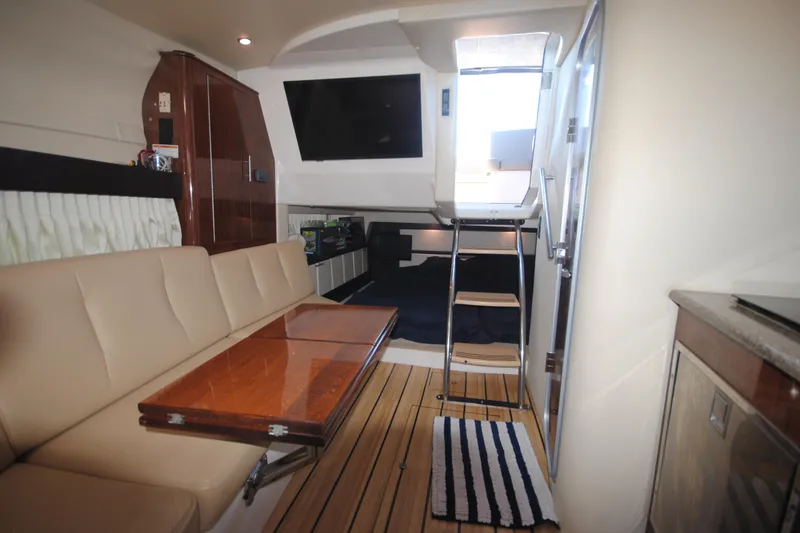 Slide: The Image of 2015 Regal 32 Express interior with beige seating, wooden table, and striped rug. - 19