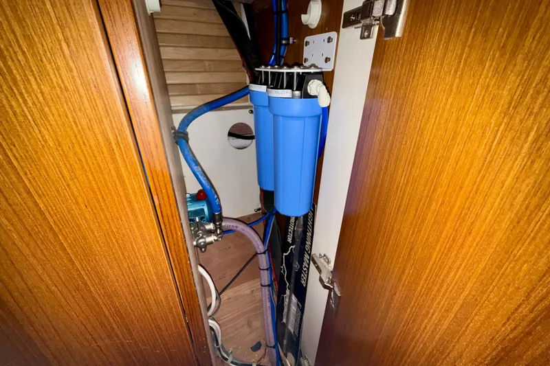 Slide: The Image of Water filtration system inside 2020 Catalina 425 yacht, featuring blue filter and wooden cabinetry. - 55