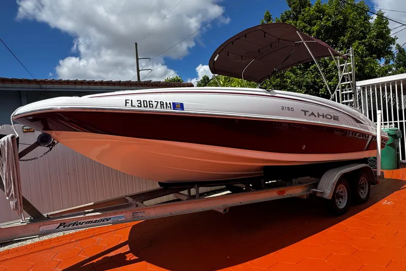 Slide: The Image of 2017 Tahoe 2150 boat on trailer, red and white, with canopy, parked outdoors. - 2
