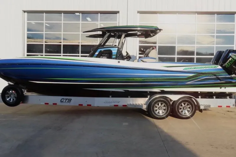 Slide: The Image of 2025 Sunsation 32 CCX boat on trailer, blue and green design, parked outside a garage. - 4