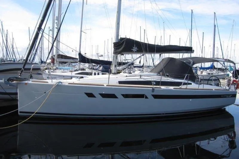 The Image of 2022 Jeanneau Sun Odyssey 349 sailboat docked in a marina, surrounded by other boats. - 0