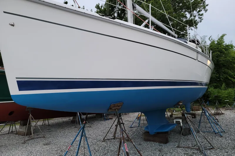 Slide: The Image of 2006 Hunter 38 sailboat on stands, white hull with blue stripe, gravel yard. - 70
