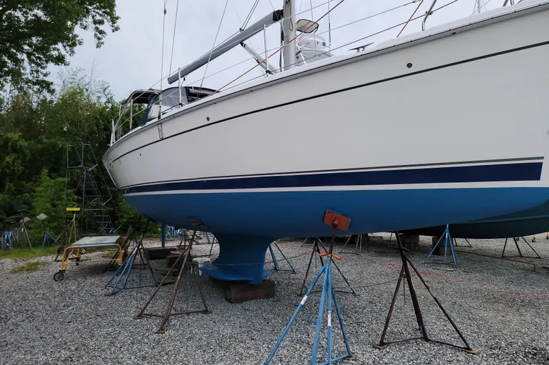 Slide: The Image of 2006 Hunter 38 sailboat on stands, white hull with blue stripe, gravel yard. - 71