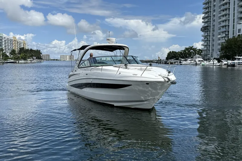 Slide: The Image of 2015 Sea Ray 370 Venture cruising in a scenic marina with modern buildings. - 2