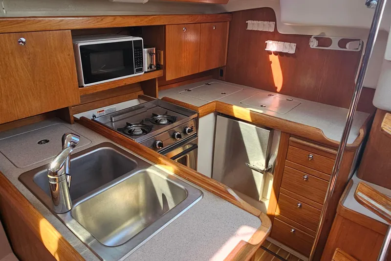 Slide: The Image of 2007 Catalina 350 yacht kitchen with stove, microwave, sink, and wooden cabinetry. - 18