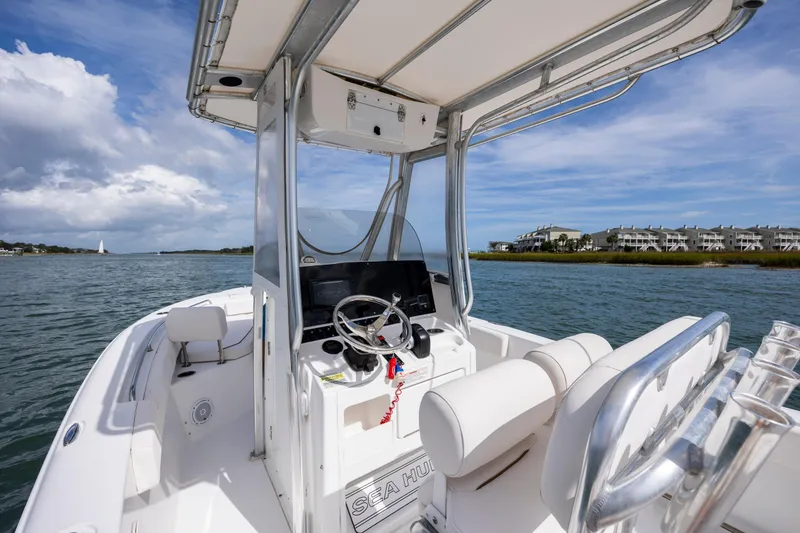 Slide: The Image of 2020 Sea Hunt Ultra 225 boat on water, featuring helm and seating, with coastal backdrop. - 15
