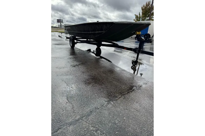Slide: The Image of 2026 Tracker Grizzly 1648 Utility boat on trailer, parked on wet pavement under cloudy skies. - 5