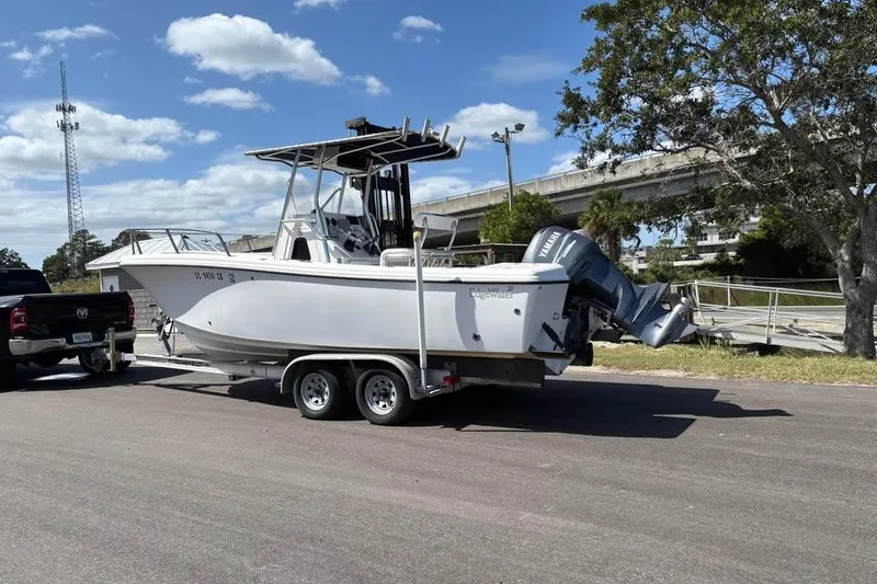 Slide: The Image of 2001 Edgewater 225CC boat on trailer, parked near a truck under a clear sky. - 2