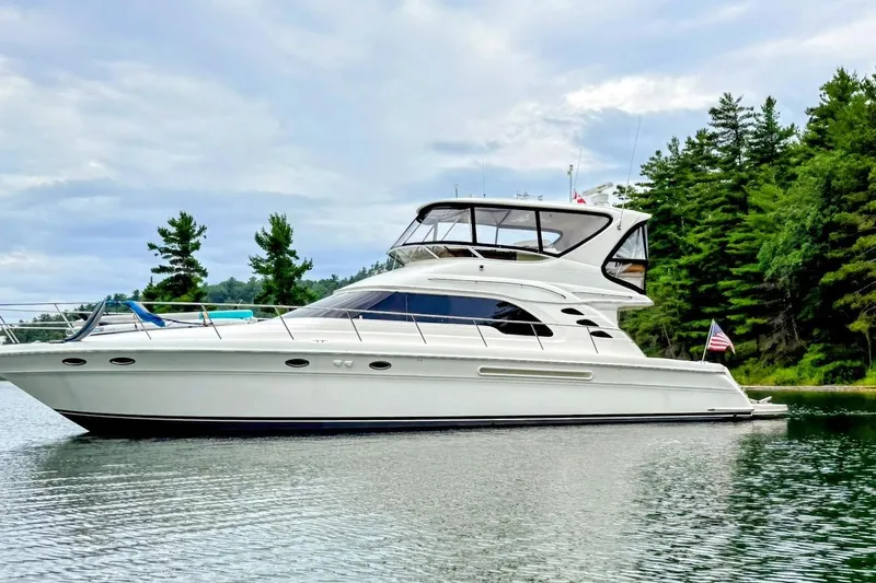Slide: The Image of 2001 Sea Ray 560 Sedan Bridge yacht on a serene lake with forested background. - 5