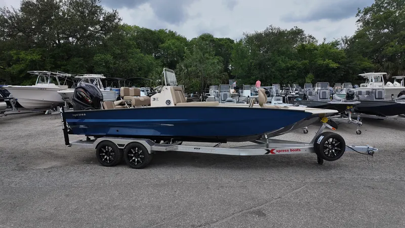 The Image of 2025 Xpress X23B Lounge boat on trailer, parked outdoors with other boats in background. - 0