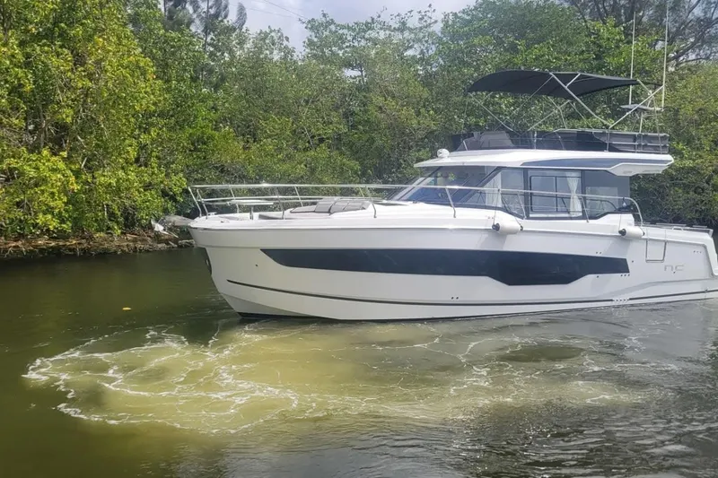 Slide: The Image of 2025 Jeanneau NC 1295 Fly yacht on clear turquoise water, with industrial backdrop. - 1