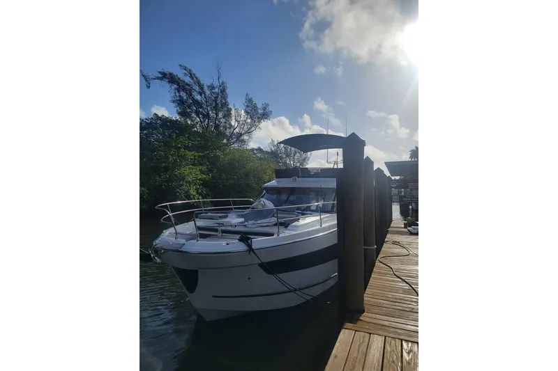 Slide: The Image of 2025 Jeanneau NC 1295 Fly yacht on clear blue water near urban skyline. - 2