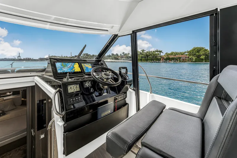 Slide: The Image of 2025 Jeanneau NC 1295 Fly cockpit with navigation screens, steering wheel, and waterfront view. - 29