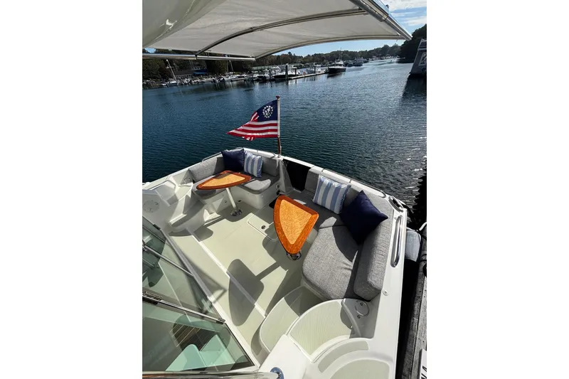 Slide: The Image of 2020 Back Cove 37 boat with cushioned seating, wooden tables, and American flag on calm water. - 16