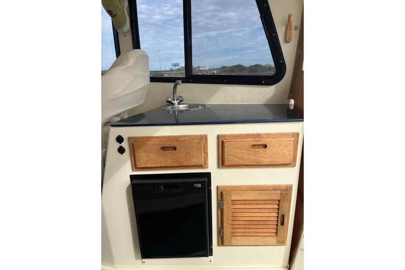 Slide: The Image of 2020 Eastern 27 Islander boat interior with sink, wooden cabinets, and window view. - 7