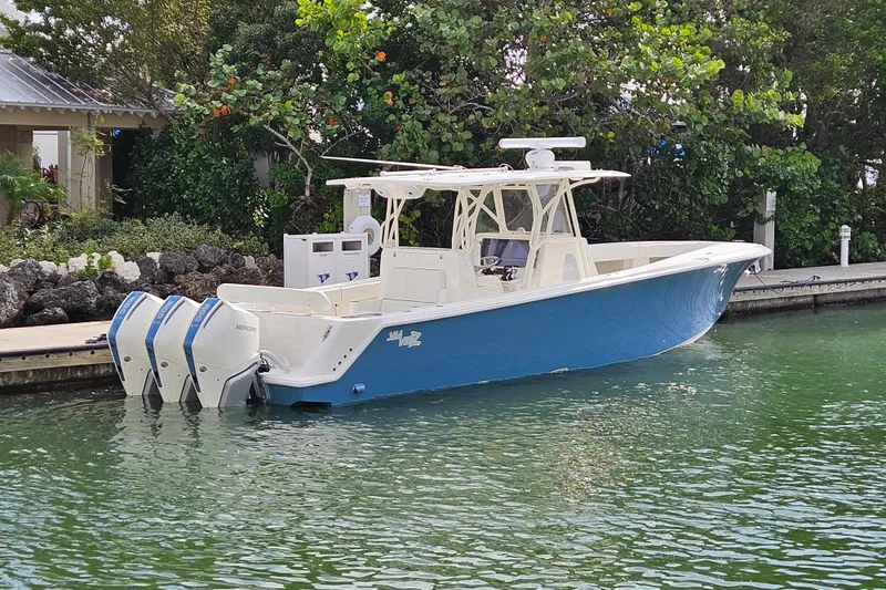 The Image of 2023 SeaVee 370z boat docked, featuring triple outboard engines, in a lush, green marina setting. - 0