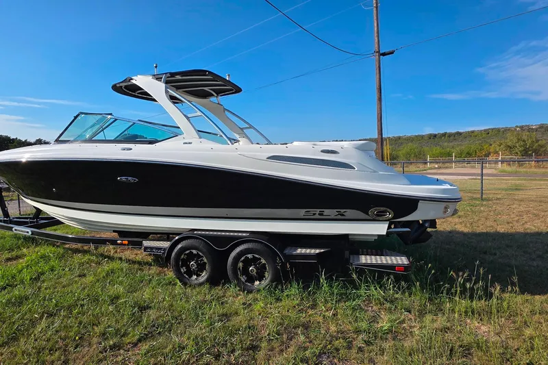 Slide: The Image of 2009 Sea Ray 270 SLX boat on trailer, parked on grassy field under clear blue sky. - 2