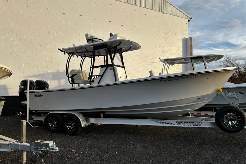 The Image of 2024 Pair Customs 24DV boat on trailer, parked outdoors near a white building. - 1