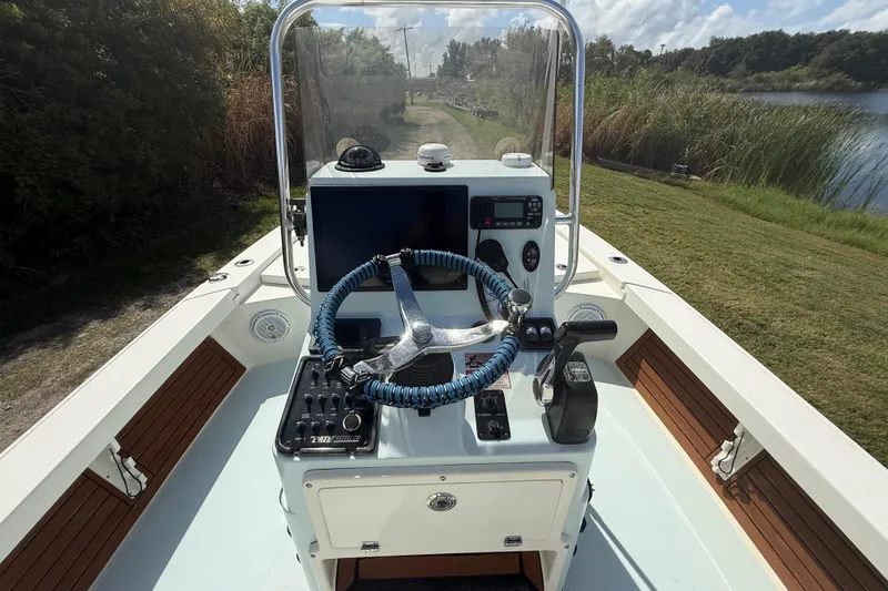 Slide: The Image of 2016 Pathfinder 2300 HPS boat console with steering wheel and controls, near grassy shoreline. - 15