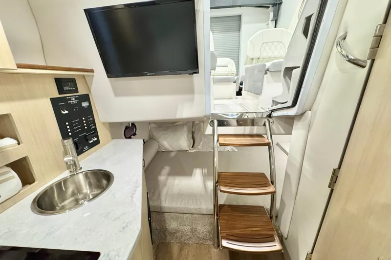 Slide: The Image of Interior of 2026 Regal 26 XO boat featuring kitchenette, TV, and wooden steps. - 12