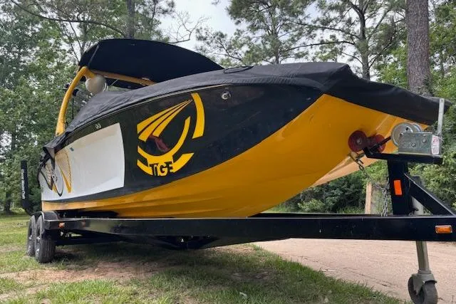 Slide: The Image of 2013 Tigé RZ4 boat in yellow and black on trailer, surrounded by trees. - 2