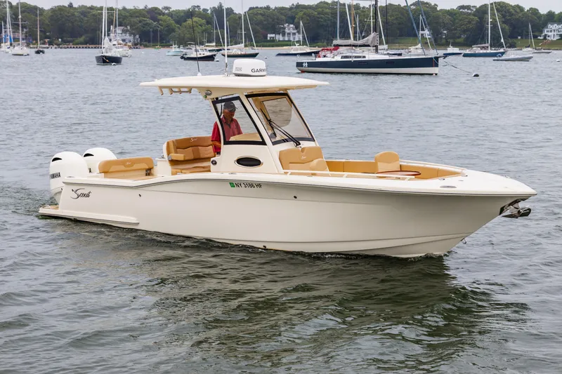 Slide: The Image of 2021 Scout 277LXF boat cruising on a calm lake with sailboats in the background. - 0