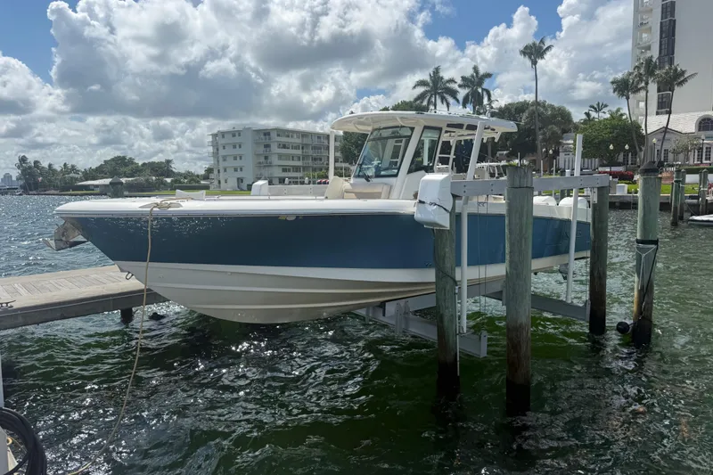 The Image of 2016 Boston Whaler 330 Outrage boat docked on a lift, with scenic waterfront backdrop. - 0