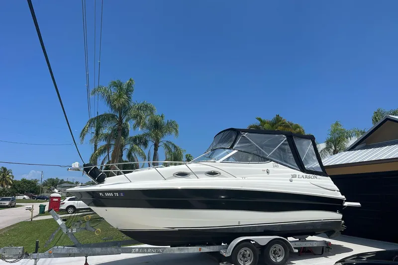 The Image of 2011 Larson Carbiro 240 boat on trailer, parked near palm trees under clear blue sky. - 1