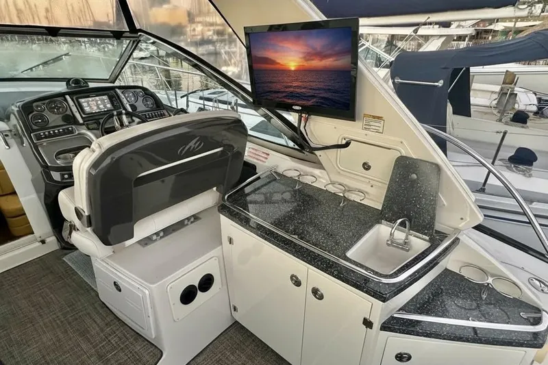 Slide: The Image of Cockpit of 2013 Monterey 400 Sport Yacht with helm, sink, and TV displaying sunset. - 5