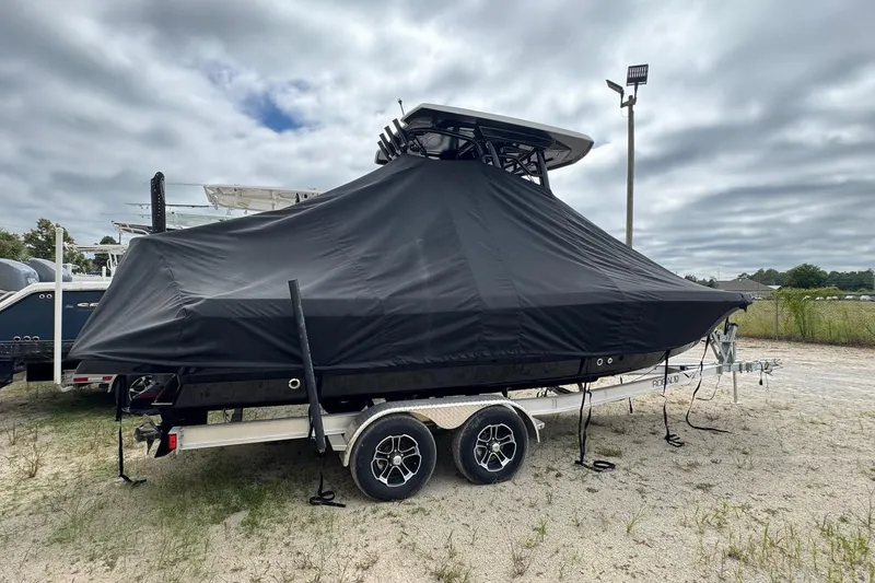 Slide: The Image of 2024 Robalo 226 Cayman boat covered on a trailer, parked outdoors under cloudy skies. - 6