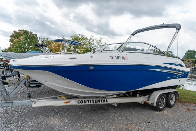 The Image of 2024 Hurricane SunDeck 217 OB boat on trailer, blue and white design, parked outdoors. - 1