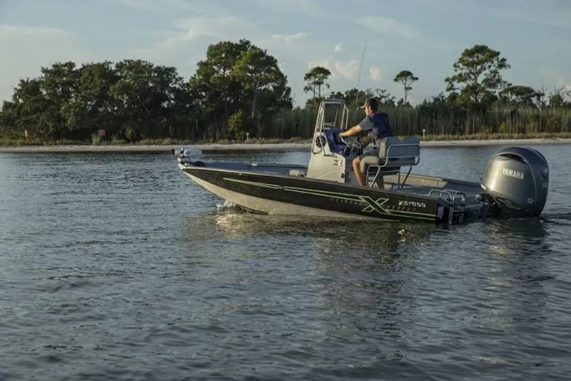 Slide: The Image of 2026 Xpress H20B Bay boat interior with camouflage seating and steering wheel, outside dealership. - 2