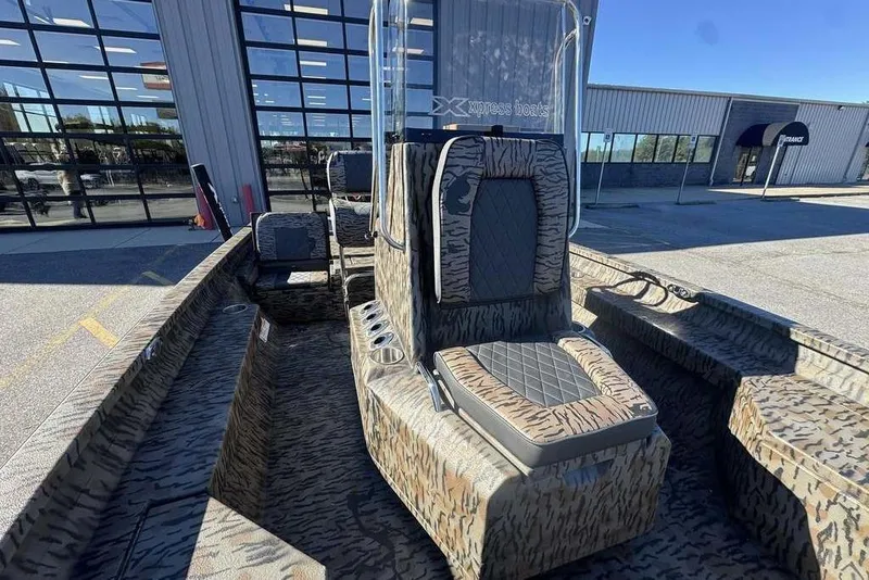Slide: The Image of 2026 Xpress H20B Bay boat with camouflage seating, parked outside a showroom. - 25