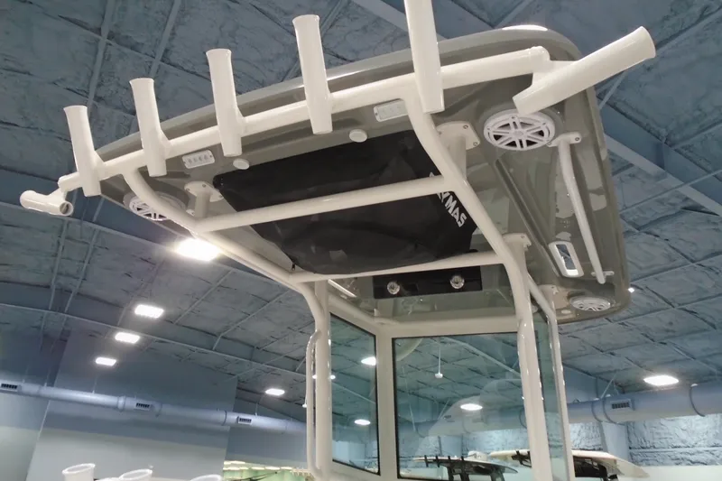 Slide: The Image of 2026 Caymas 24 HB boat T-top with rod holders and speakers in showroom. - 14