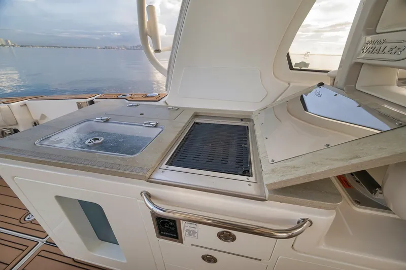 Slide: The Image of 2020 Boston Whaler 380 Realm boat kitchen with sink and grill, overlooking serene water. - 22