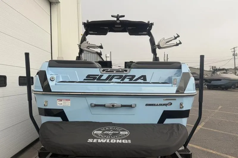 Slide: The Image of 2025 Supra SL 575 boat, rear view, light blue, parked outdoors. - 2
